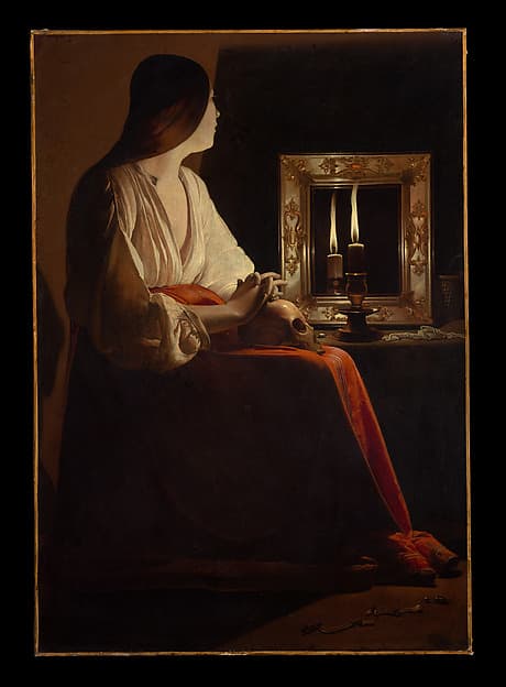 A woman sitting in stillness beside a single candle flame, the background sinking into pure black